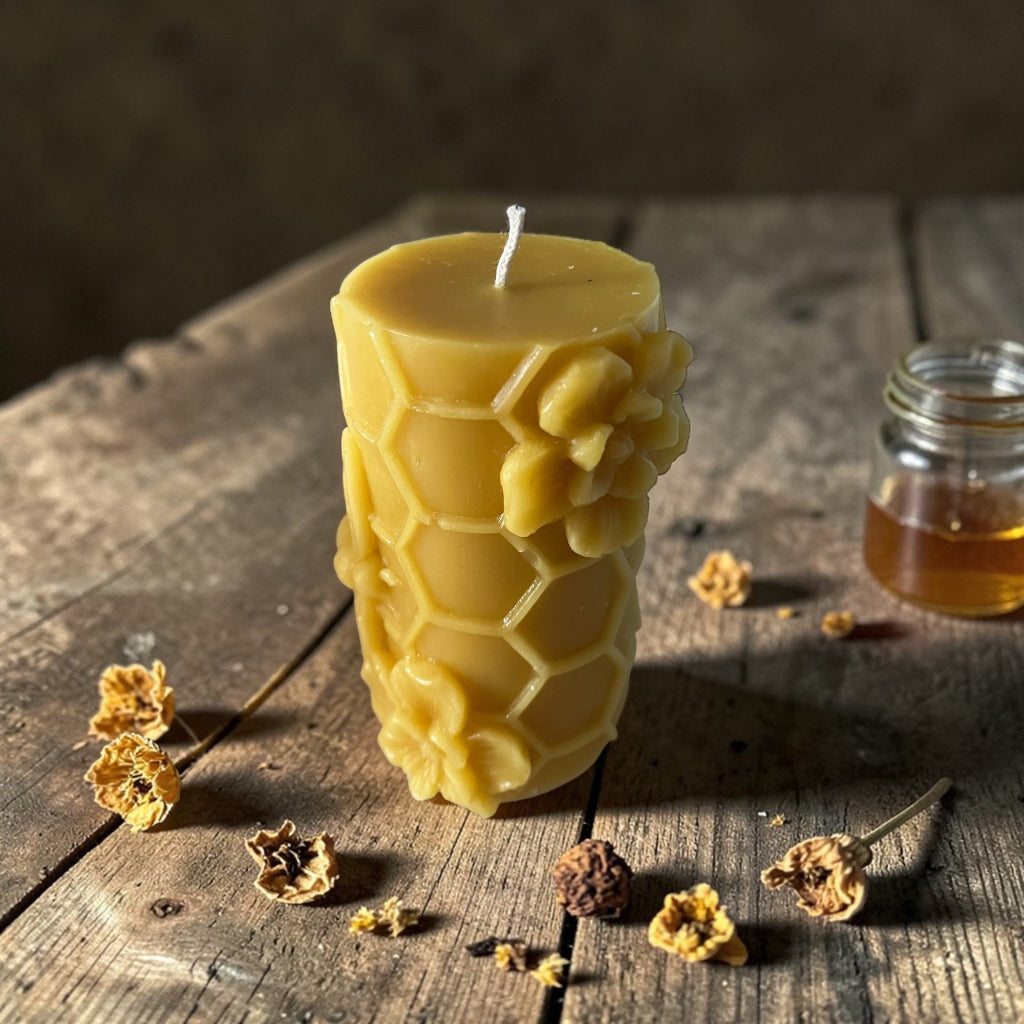 Beeswax candle with honeycomb design on a wooden surface with honey and flowers.