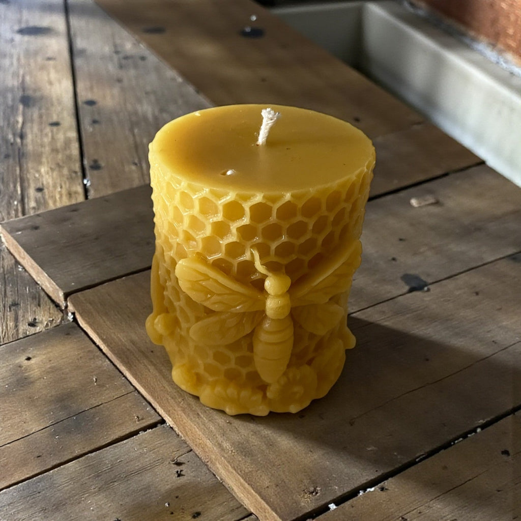 Yellow beeswax candle with honeycomb and bee design on a wooden surface