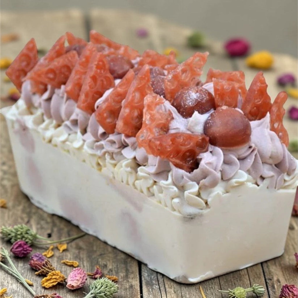 Rectangular handmade honey and buttermilk soap loaf on a wooden surface with flowers.