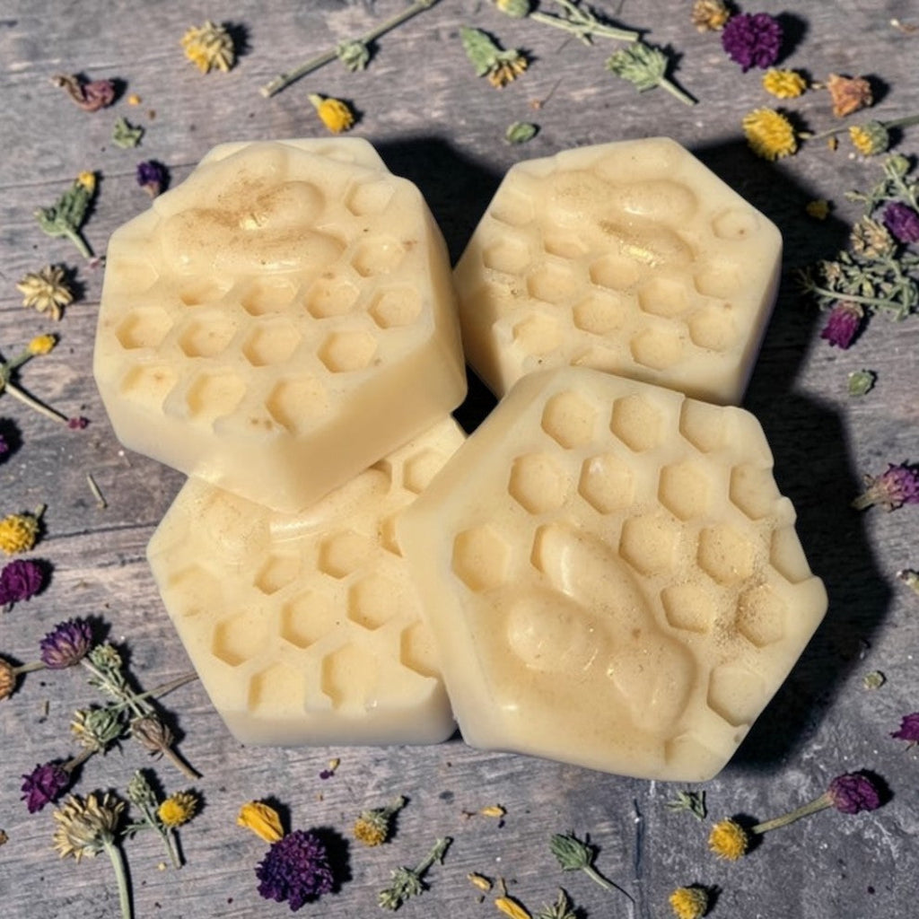 Four hexagonal beeswax luxurious lotion bars on a wooden surface with flowers around them