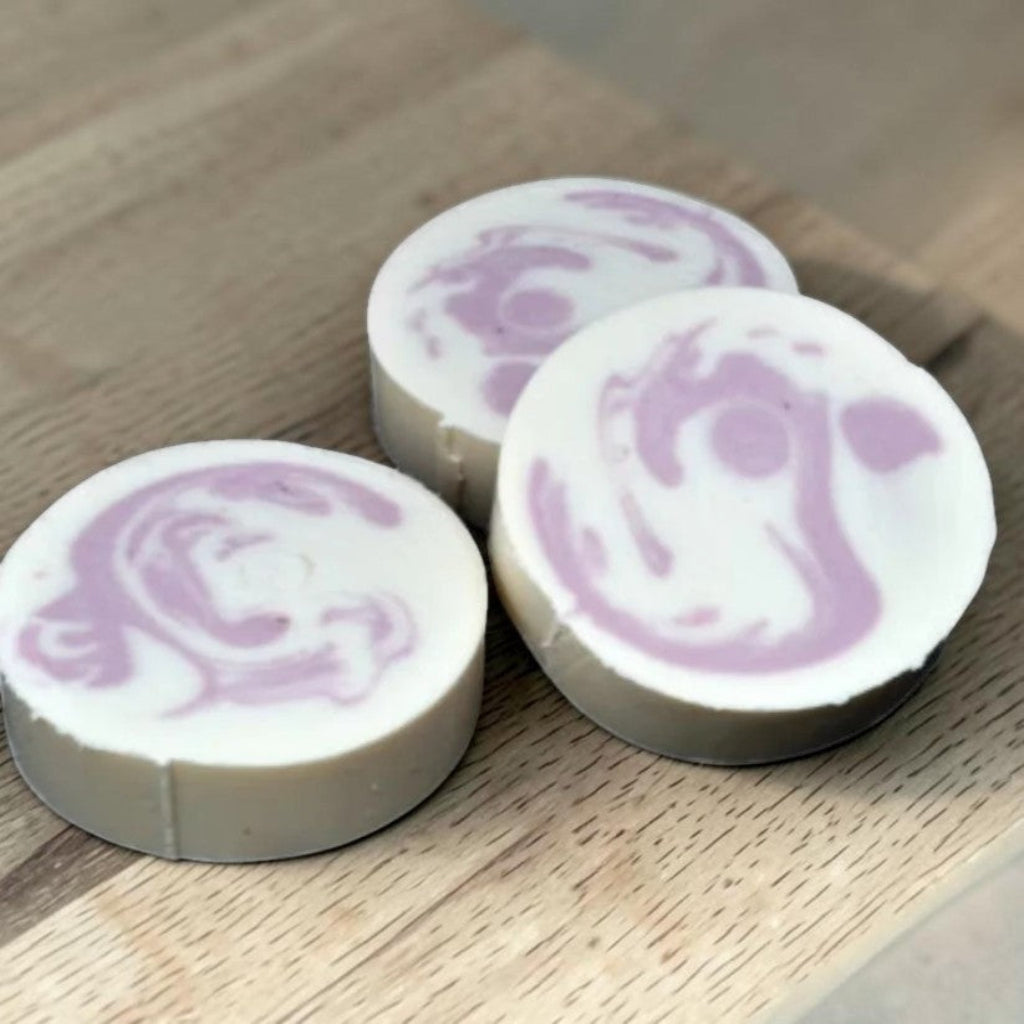 Three round shampoo soap bars with pink swirl patterns on a wooden surface
