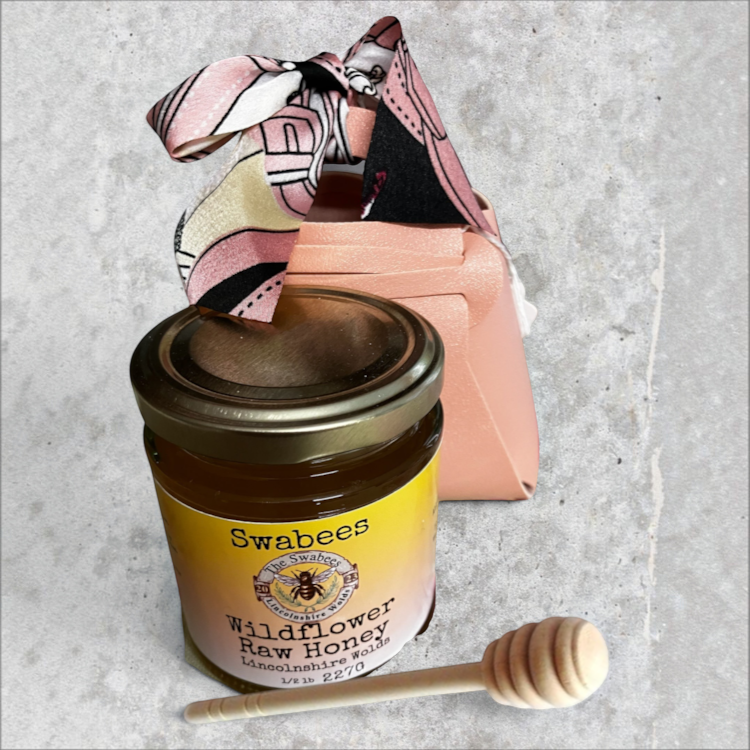 Swabees Wildflower Raw Honey jar with wooden dipper and blush-pink faux leather gift bag with patterned ribbon