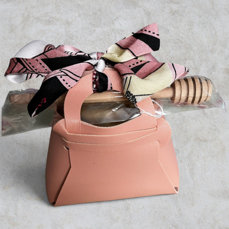 Swabees wildflower raw honey gift set in a blush-pink faux leather bag with a wooden dipper and patterned ribbon.